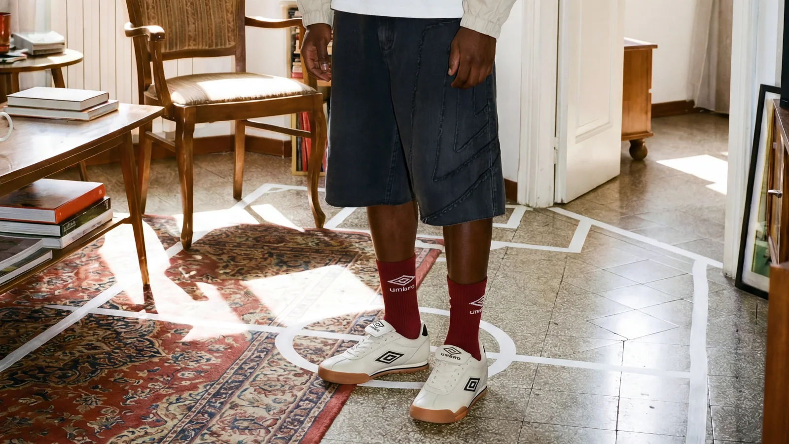 White Umbro footwear with red branded socks, shorts and graphic football pitch markings across the floor